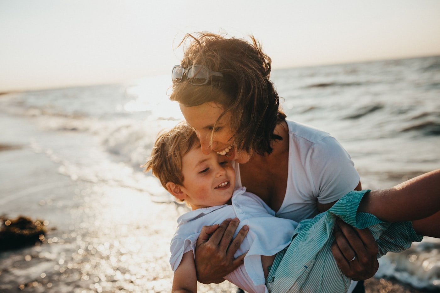 A parent lifting their child into golden light by the sea